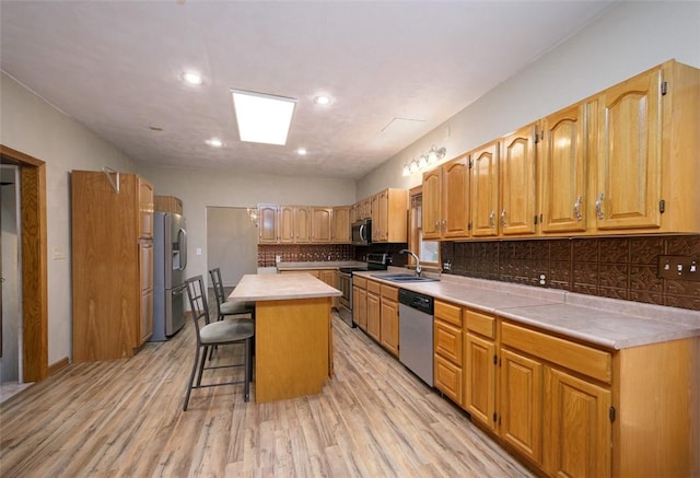 kitchen with a center island, backsplash, light wood-type flooring, appliances with stainless steel finishes, and a kitchen bar