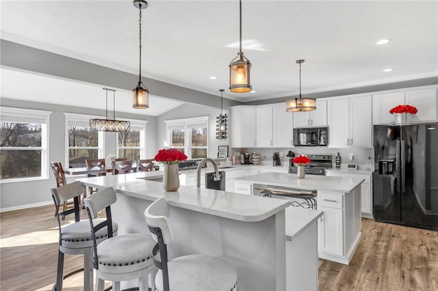 kitchen with black appliances, light hardwood / wood-style floors, hanging light fixtures, and a kitchen island with sink