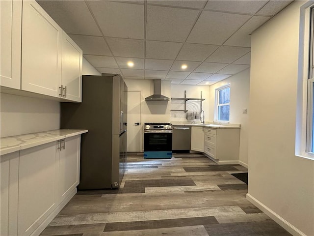 kitchen featuring wall chimney range hood, sink, appliances with stainless steel finishes, dark hardwood / wood-style flooring, and white cabinetry