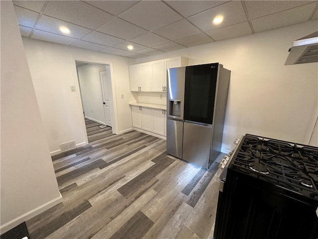 kitchen featuring a paneled ceiling, black range with gas cooktop, wood-type flooring, stainless steel fridge with ice dispenser, and white cabinetry