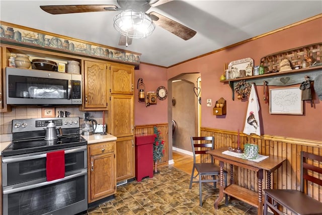 kitchen with ceiling fan, wood walls, crown molding, decorative backsplash, and appliances with stainless steel finishes