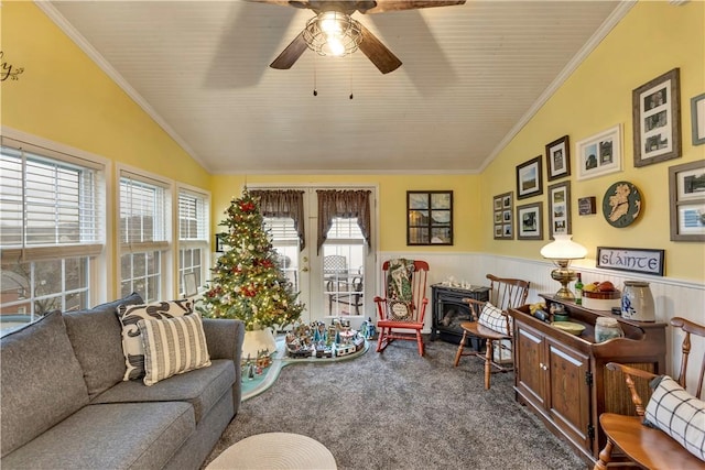 carpeted living room with a wood stove, vaulted ceiling, ceiling fan, and crown molding