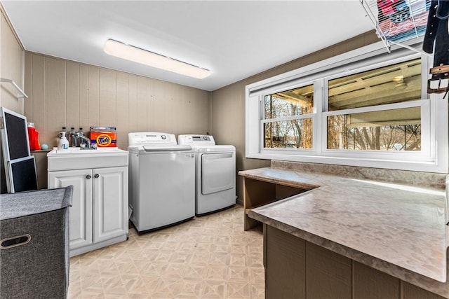 clothes washing area featuring wooden walls, sink, cabinets, and independent washer and dryer