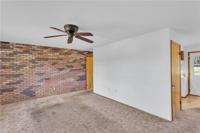 carpeted empty room with ceiling fan and brick wall