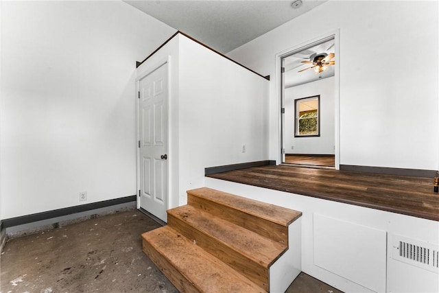 staircase with ceiling fan and concrete floors