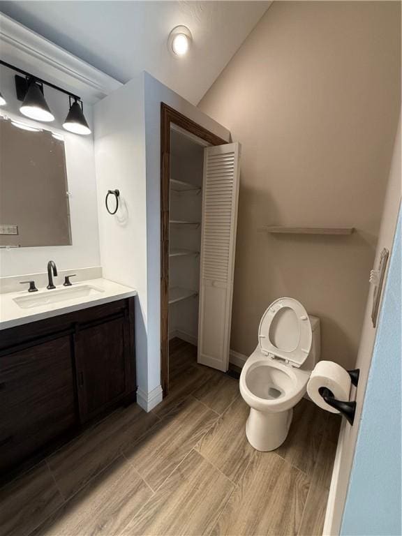 bathroom with hardwood / wood-style floors, vanity, toilet, and lofted ceiling