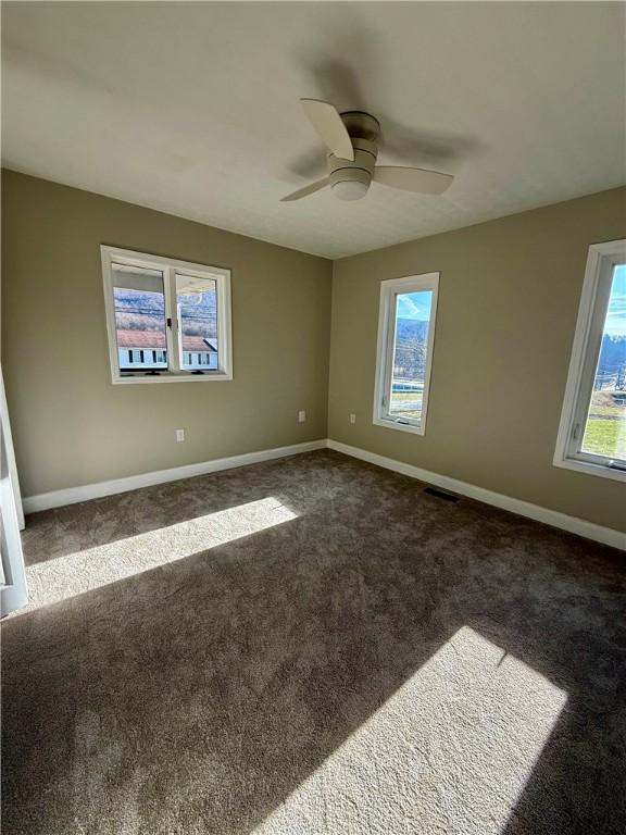 unfurnished room with a wealth of natural light and dark carpet