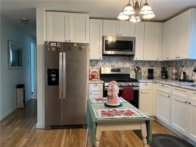 kitchen with hanging light fixtures, tasteful backsplash, light hardwood / wood-style floors, white cabinetry, and stainless steel appliances