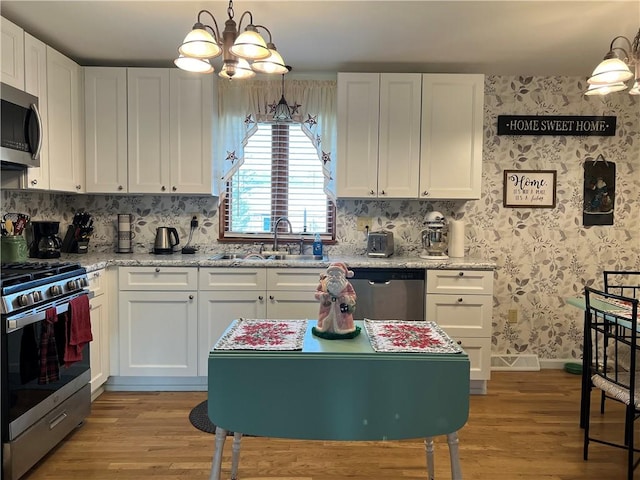 kitchen with appliances with stainless steel finishes, sink, light hardwood / wood-style floors, white cabinetry, and hanging light fixtures