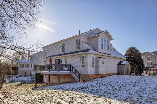 snow covered rear of property featuring a deck and a storage unit