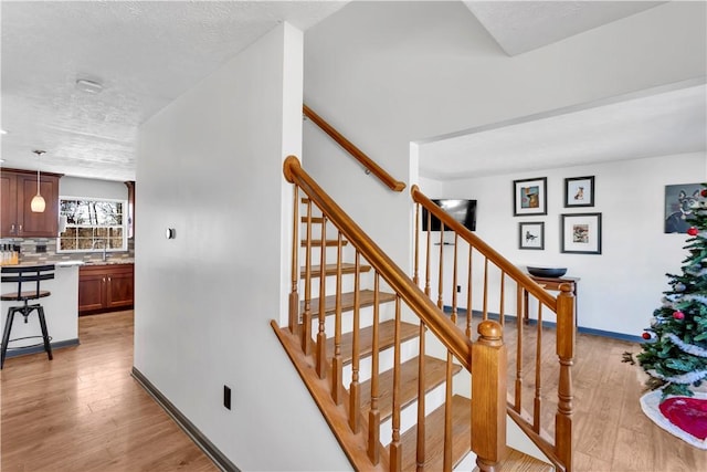 stairs with a textured ceiling, wood-type flooring, and sink