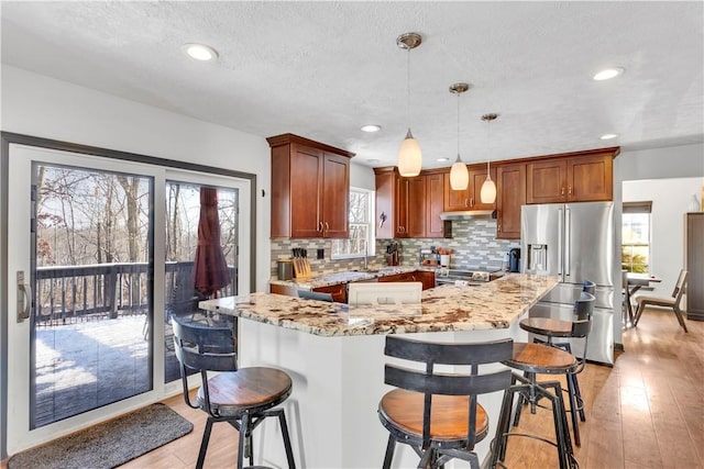 kitchen featuring light stone countertops, a textured ceiling, decorative light fixtures, appliances with stainless steel finishes, and light wood-type flooring