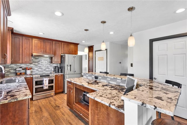 kitchen with light stone counters, stainless steel appliances, sink, light hardwood / wood-style floors, and hanging light fixtures