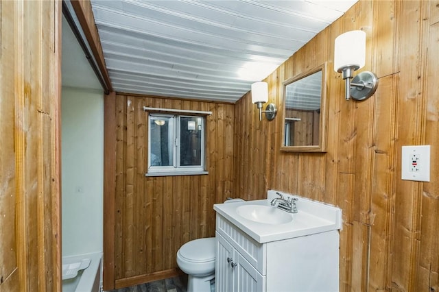 bathroom with vanity, toilet, and wood walls