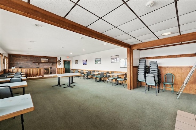 rec room featuring carpet, a paneled ceiling, a brick fireplace, and wooden walls