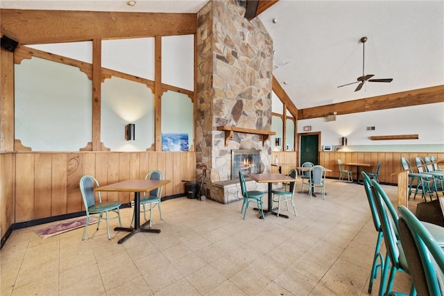 interior space featuring ceiling fan, wood walls, a stone fireplace, and high vaulted ceiling