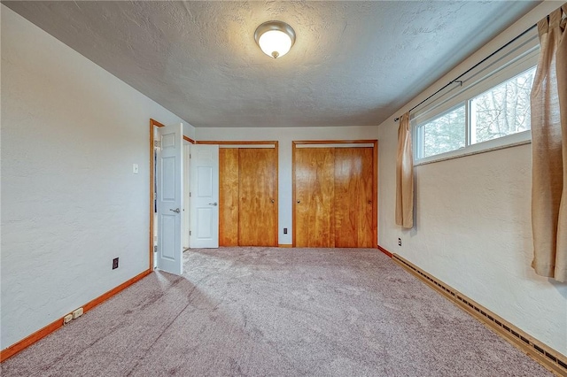 unfurnished bedroom featuring a textured ceiling, carpet floors, and multiple closets