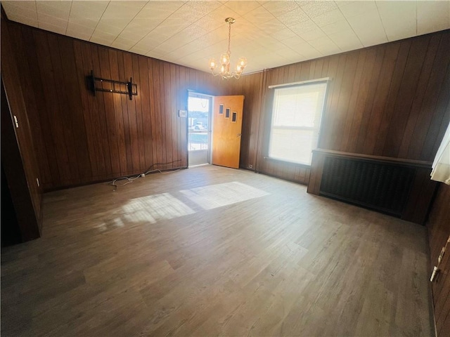 empty room with hardwood / wood-style floors, wood walls, and an inviting chandelier