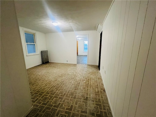 empty room with radiator heating unit, a textured ceiling, and wood walls