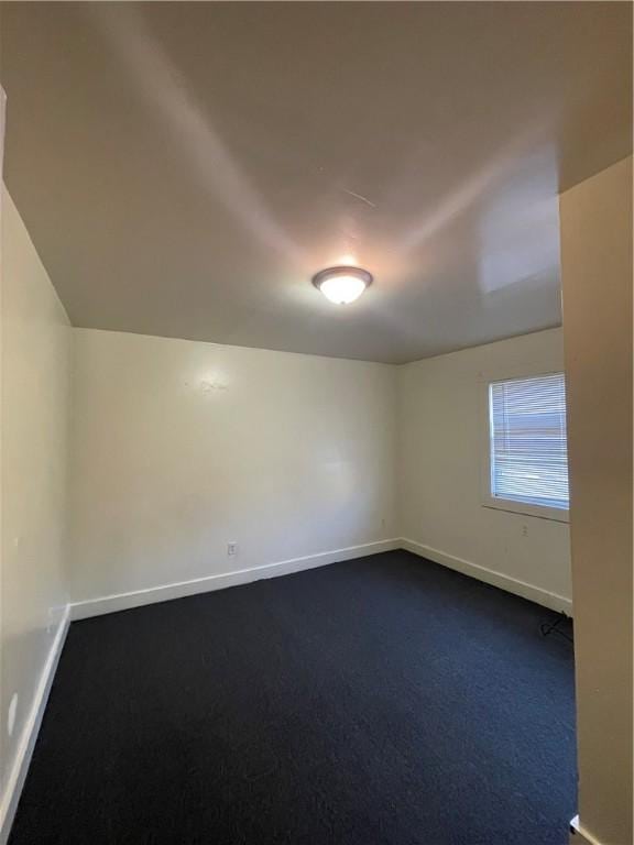 empty room with dark colored carpet and vaulted ceiling