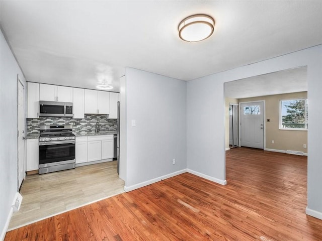 kitchen with sink, decorative backsplash, appliances with stainless steel finishes, light hardwood / wood-style floors, and white cabinetry