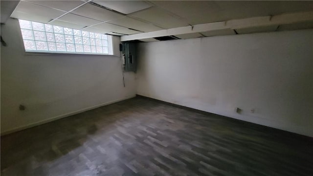 basement featuring dark wood-type flooring, a paneled ceiling, and electric panel