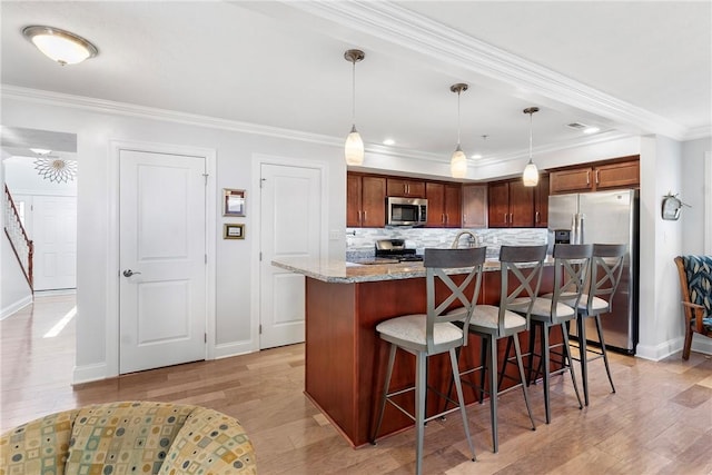 kitchen with light stone countertops, appliances with stainless steel finishes, light hardwood / wood-style flooring, hanging light fixtures, and an island with sink