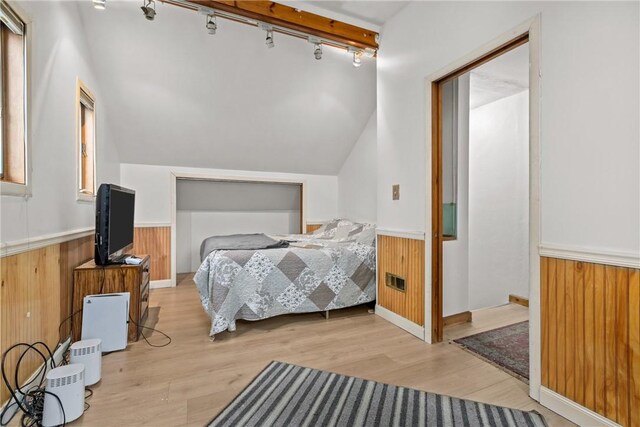 bedroom with vaulted ceiling, light hardwood / wood-style floors, rail lighting, and wood walls