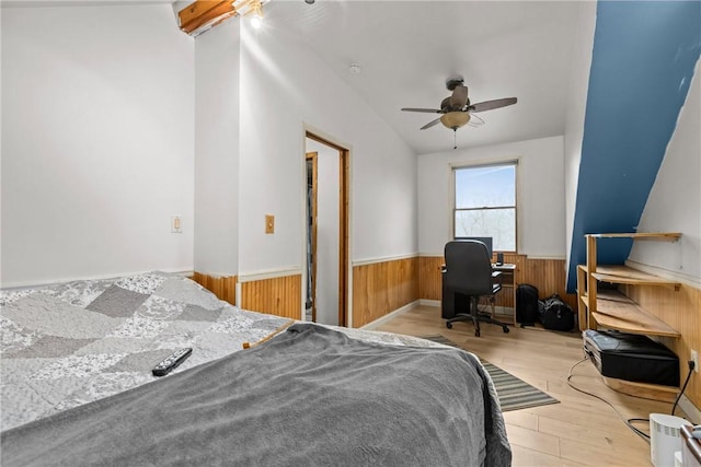 bedroom with vaulted ceiling, wooden walls, ceiling fan, and light wood-type flooring