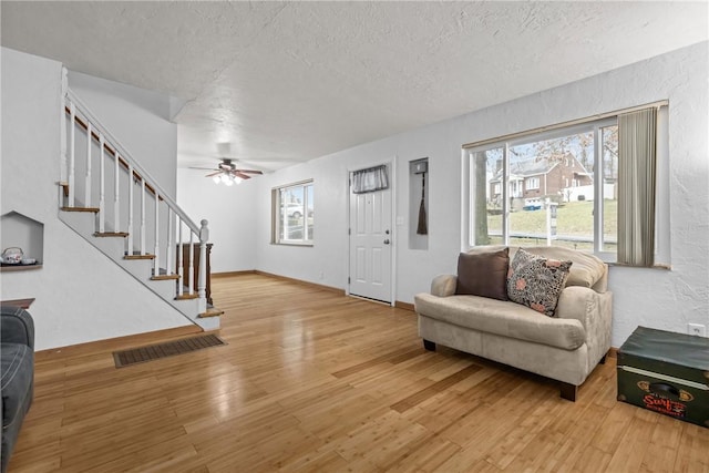 living room featuring ceiling fan, a textured ceiling, and light wood-type flooring