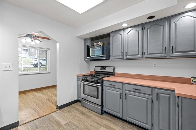 kitchen featuring stainless steel gas stove, light hardwood / wood-style flooring, gray cabinetry, and ceiling fan