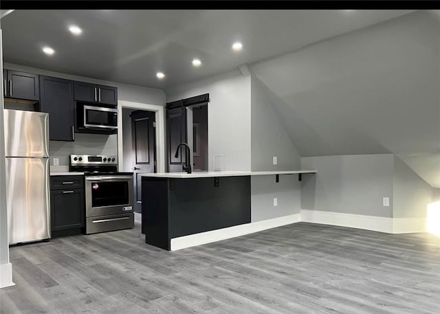 kitchen featuring a barn door, light hardwood / wood-style flooring, vaulted ceiling, a breakfast bar, and appliances with stainless steel finishes