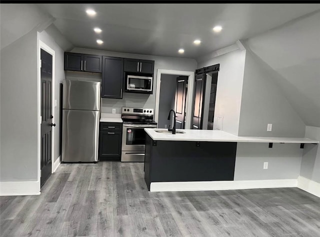 kitchen with sink, stainless steel appliances, a kitchen breakfast bar, kitchen peninsula, and light hardwood / wood-style floors