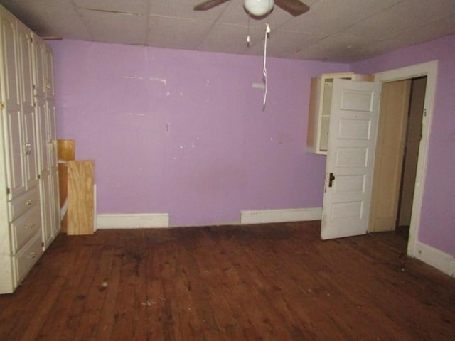 empty room with dark hardwood / wood-style flooring, a drop ceiling, and ceiling fan