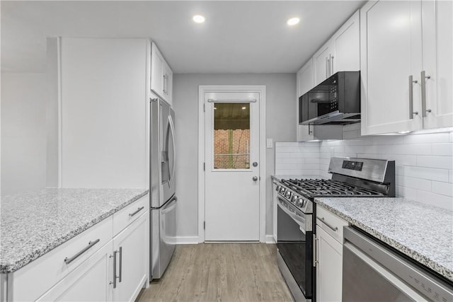 kitchen with light stone countertops, light wood-type flooring, stainless steel appliances, and white cabinetry