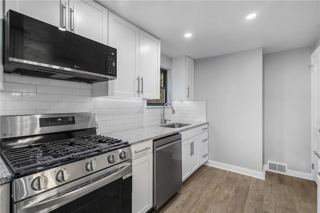 kitchen with sink, light stone countertops, appliances with stainless steel finishes, light hardwood / wood-style floors, and white cabinetry