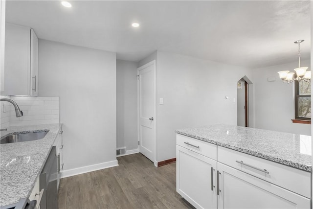 kitchen with light stone countertops, white cabinetry, sink, dark hardwood / wood-style floors, and pendant lighting