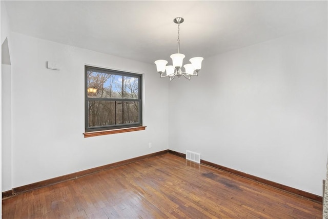 unfurnished room with a chandelier and dark wood-type flooring