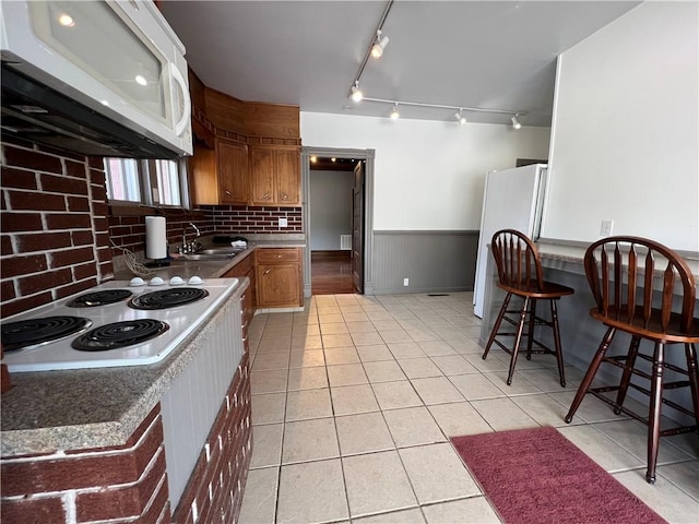 kitchen featuring white appliances, sink, tasteful backsplash, light tile patterned flooring, and a kitchen bar