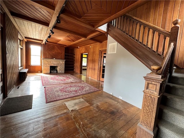 unfurnished living room with beam ceiling, wooden ceiling, wooden walls, a fireplace, and hardwood / wood-style flooring