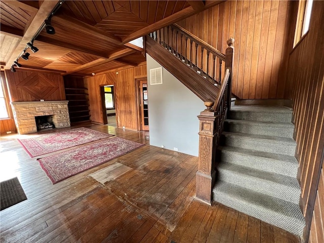 staircase featuring beam ceiling, wooden walls, a fireplace, wood ceiling, and hardwood / wood-style flooring