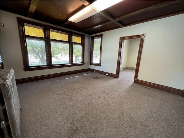 unfurnished room featuring radiator, beamed ceiling, and carpet floors