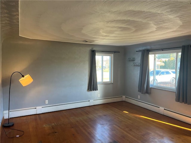 empty room featuring a wealth of natural light, dark hardwood / wood-style flooring, and a baseboard heating unit