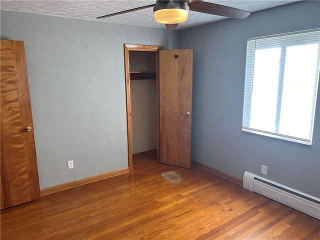 unfurnished bedroom with ceiling fan, a baseboard heating unit, a textured ceiling, a closet, and hardwood / wood-style flooring