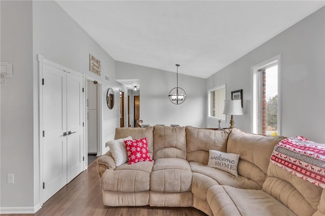 living room with an inviting chandelier, dark wood-type flooring, and vaulted ceiling