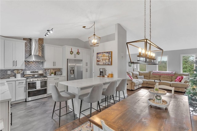 kitchen featuring white cabinetry, a center island, wall chimney range hood, a kitchen breakfast bar, and appliances with stainless steel finishes