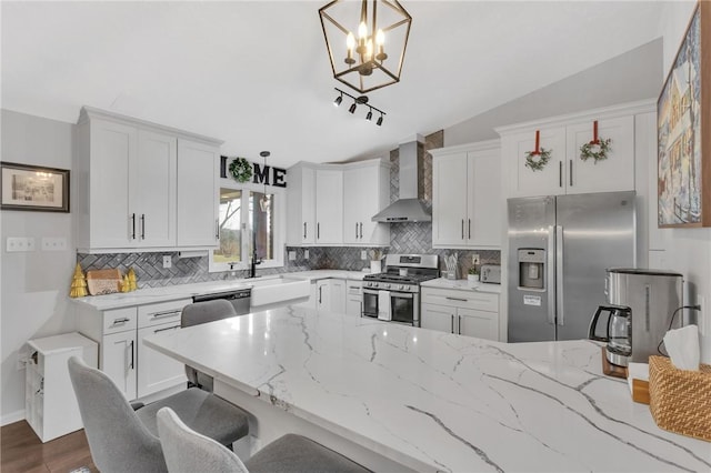 kitchen with wall chimney exhaust hood, stainless steel appliances, white cabinetry, hanging light fixtures, and lofted ceiling