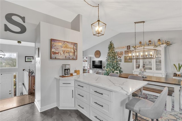 kitchen featuring light stone countertops, white cabinets, decorative light fixtures, and lofted ceiling