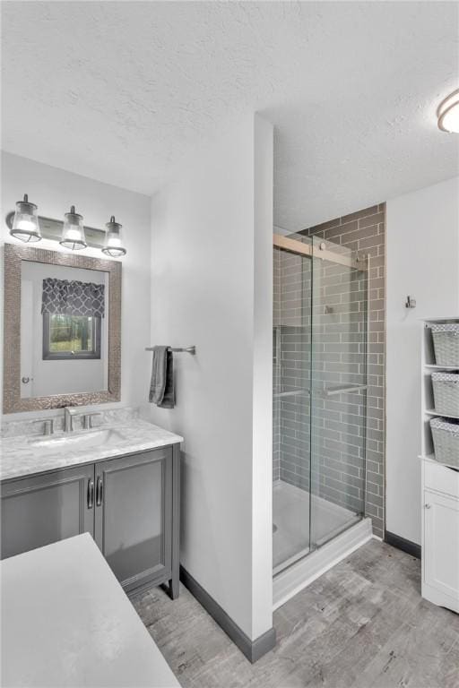 bathroom with hardwood / wood-style floors, vanity, a shower with shower door, and a textured ceiling