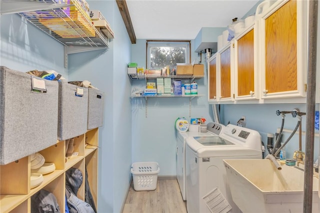 clothes washing area featuring cabinets, light wood-type flooring, washing machine and dryer, and sink